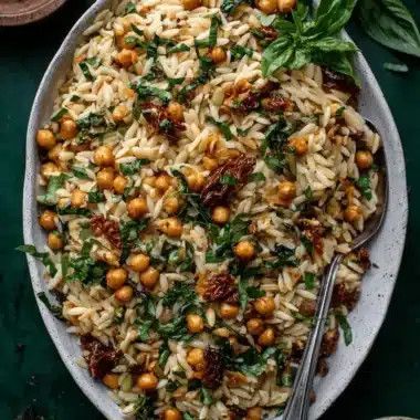 Quick & Easy Lemon Orzo Pasta Salad 3 A vibrant Lemon Orzo Pasta Salad with golden orzo, bright chickpeas, rich sun-dried tomatoes, and fresh basil, served in a ceramic dish on a dark green surface, ready to be enjoyed.