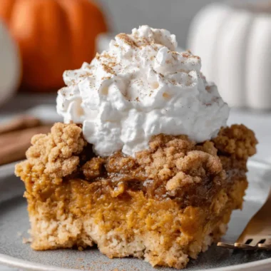 Foolproof Pumpkin Dump Cake Recipe 3 A delicious slice of pumpkin dump cake with a golden crumble topping and a dollop of whipped cream on a rustic grey plate, ready to be enjoyed.