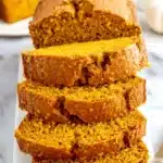 The Ultimate Foolproof Pumpkin Bread 5 Stacked slices and loaves of moist, vibrant orange pumpkin bread on a white plate with milk, ready to be enjoyed.