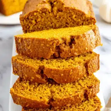 The Ultimate Foolproof Pumpkin Bread 4 Stacked slices and loaves of moist, vibrant orange pumpkin bread on a white plate with milk, ready to be enjoyed.
