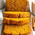 Amazing Foolproof Pumpkin Bread Recipe 8 Close-up of moist, sliced pumpkin bread on a rustic wooden cutting board, lightly dusted with powdered sugar.