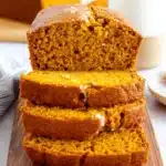 Amazing Ultimate Moist Pumpkin Bread 6 Deliciously sliced pumpkin bread on a rustic wooden board, revealing its moist, spiced interior, with a whole loaf and milk in the background.