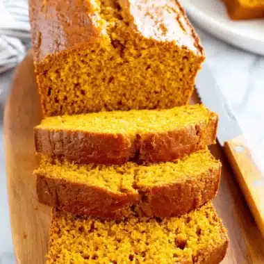 Amazing Foolproof Pumpkin Bread Recipe 4 Freshly sliced pumpkin bread on a wooden cutting board, revealing its moist, vibrant orange interior.
