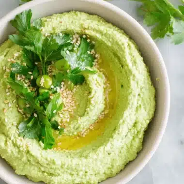 Amazing Edamame Hummus: Quick & Creamy Recipe 4 A vibrant green bowl of creamy edamame hummus, garnished with fresh parsley, toasted sesame seeds, and a drizzle of olive oil on a marble surface.