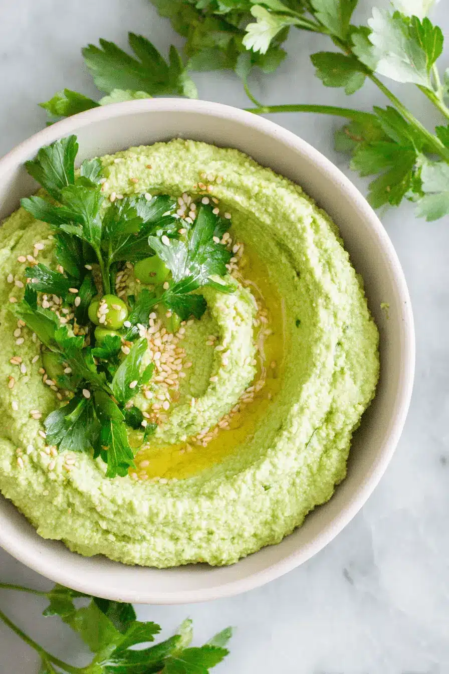 Amazing Edamame Hummus: Quick & Creamy Recipe 2 A vibrant green bowl of creamy edamame hummus, garnished with fresh parsley, toasted sesame seeds, and a drizzle of olive oil on a marble surface.