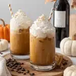 Amazing Homemade Pumpkin Spice Latte 6 Two iced pumpkin spice lattes with whipped cream, cinnamon, and autumnal decor on a rustic wooden board.