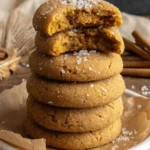 The Ultimate Chewy Pumpkin Cookies 5 A tempting stack of freshly baked pumpkin cookies on a speckled white plate, with one broken in half to show its soft, chewy interior.