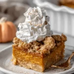 Wonderful Foolproof Pumpkin Dump Cake Recipe 7 Close-up of a delicious slice of pumpkin dump cake recipe on a white plate, topped with whipped cream and a golden-brown streusel.