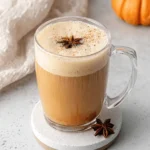 Luxurious Homemade Pumpkin Chai Latte 5 A close-up of a warm pumpkin chai latte in a clear mug, topped with frothy foam, cinnamon, and star anise, surrounded by autumn spices and a small orange pumpkin.