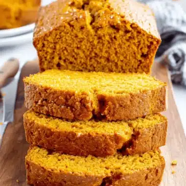 Amazing Pumpkin Bread: Simple & Moist Loaf 4 Freshly baked pumpkin bread loaf, sliced on a rustic wooden board, showing its moist texture, rich orange color, and sparkling sugar topping.