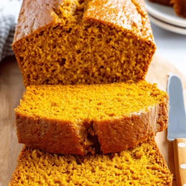 Amazing Fail-Proof Pumpkin Bread Recipe 4 Sliced golden-brown pumpkin bread on a wooden cutting board with a knife, highlighting its moist texture.