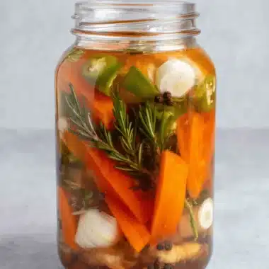 Powerful Fire Cider Recipe for Winter Wellness 4 A close-up of a glass jar filled with vibrant ingredients for a homemade fire cider recipe, featuring carrots, jalapeños, garlic, and rosemary in a rich amber liquid.