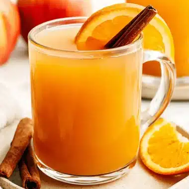 Amazing Homemade Apple Cider Recipe 3 A close-up of a glass mug filled with warm, spiced apple cider, garnished with an orange slice and cinnamon stick, suggesting a delicious apple cider recipe.