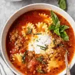 Easy One-Pot Lasagna Soup 9 Close-up overhead view of a hearty bowl of homemade lasagna soup garnished with ricotta and fresh basil.