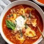 The Ultimate One-Pot Lasagna Soup 7 Close-up of a hearty bowl of Lasagna Soup with farfalle pasta, ground meat, and fresh basil on a rustic wooden surface.