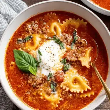 The Ultimate One-Pot Lasagna Soup 4 Close-up of a hearty bowl of Lasagna Soup with farfalle pasta, ground meat, and fresh basil on a rustic wooden surface.