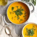 Ultimate Butternut Squash Soup Recipes: Easy Comfort 9 Top-down view of two bowls of vibrant orange butternut squash soup, garnished with parsley, served with olive oil, pumpkin seeds, and sage on a white marble surface.