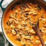 Amazing Creamy Tortellini Soup 6 Close-up of hearty, creamy tortellini soup with meat and spinach in a dark teal Dutch oven, ready to serve.
