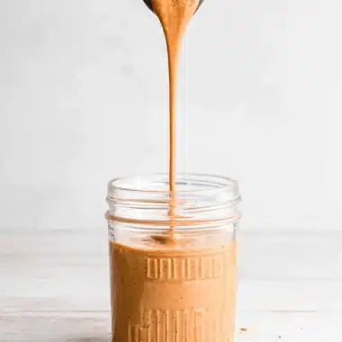 Amazing Easy Pumpkin Spice Sauce for Coffee 3 Thick, creamy light brown substance, visually resembling nut butter, being poured into a mason jar, prepared as a base for a rich pumpkin spice sauce for coffee.