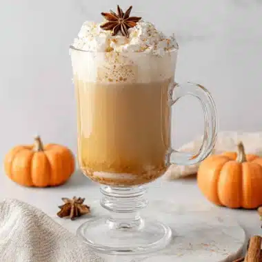 Ultimate Pumpkin Chai Latte: Easy Homemade Recipe 3 A beautifully styled pumpkin chai latte topped with whipped cream, star anise, and cinnamon, surrounded by mini pumpkins and spices on a marble slab.