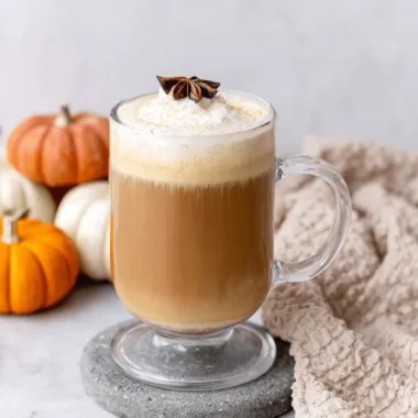 Wonderful Homemade Pumpkin Chai Latte 3 A cozy pumpkin chai latte in a clear glass mug with whipped cream, star anise, and decorative fall pumpkins.